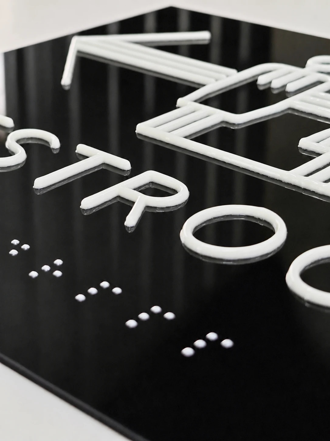 Accessible Restroom Directional Tactile Sign — Close view showing raised RESTROOM lettering, part of the person graphics, and white tactile dots.