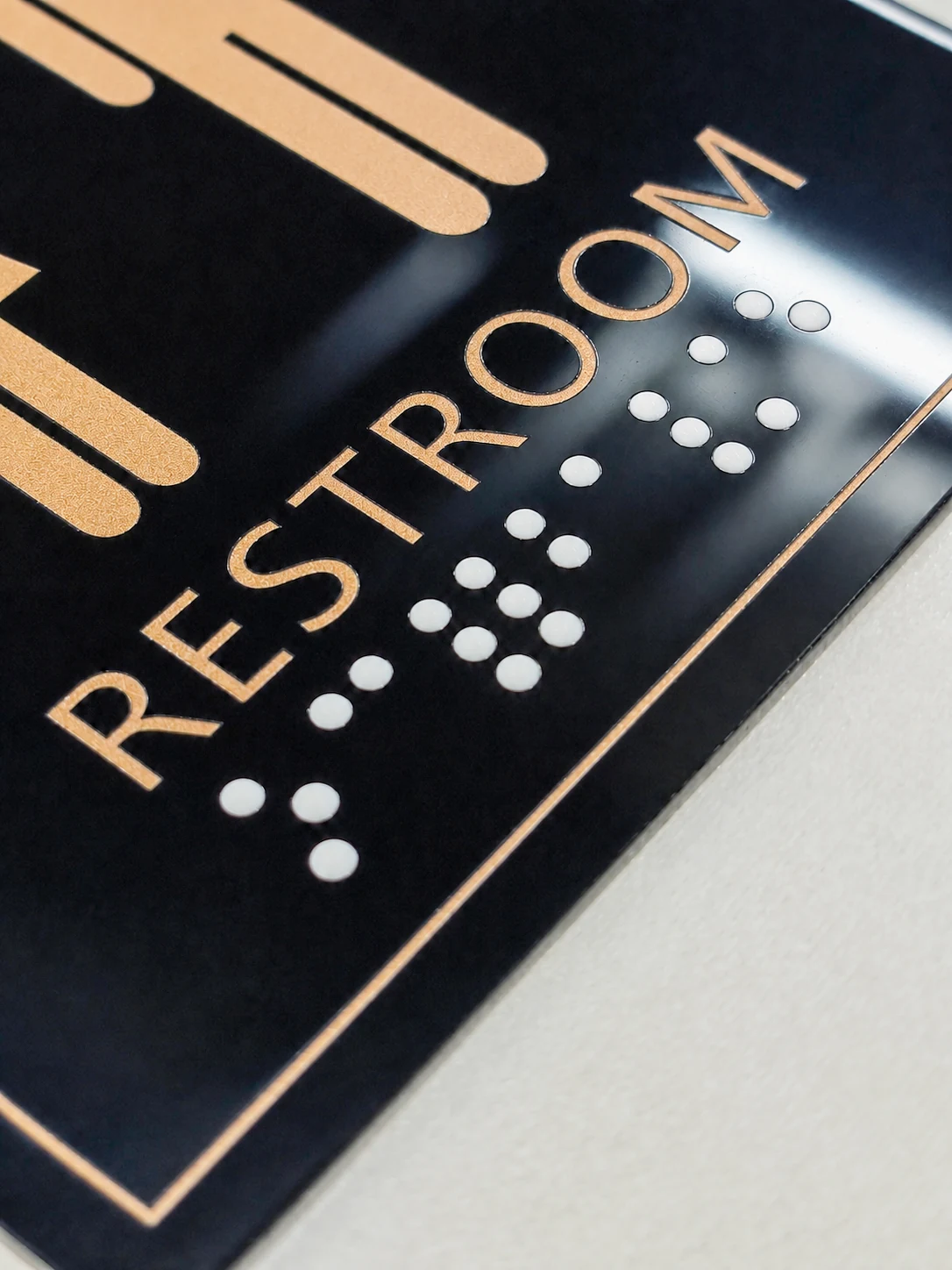 Black and Gold Resin Braille Restroom Sign — Close view of the raised RESTROOM lettering, white tactile dots, and black panel edge.