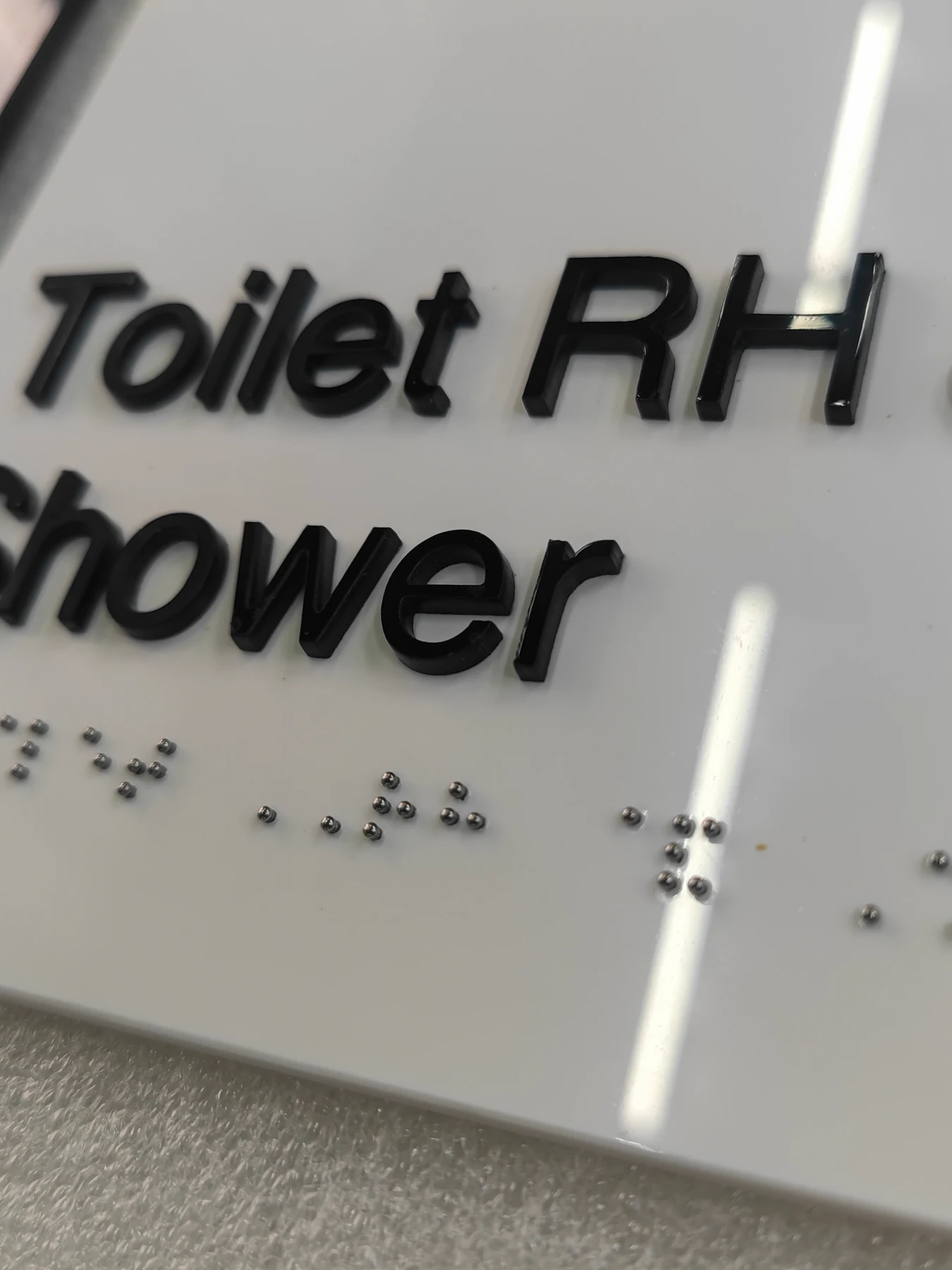 Interior Signs with 304 Stainless Steel Braille Studs — Close view of the completed white panel with raised black Toilet RH & Shower text and silver 304 stainless steel Braille studs.