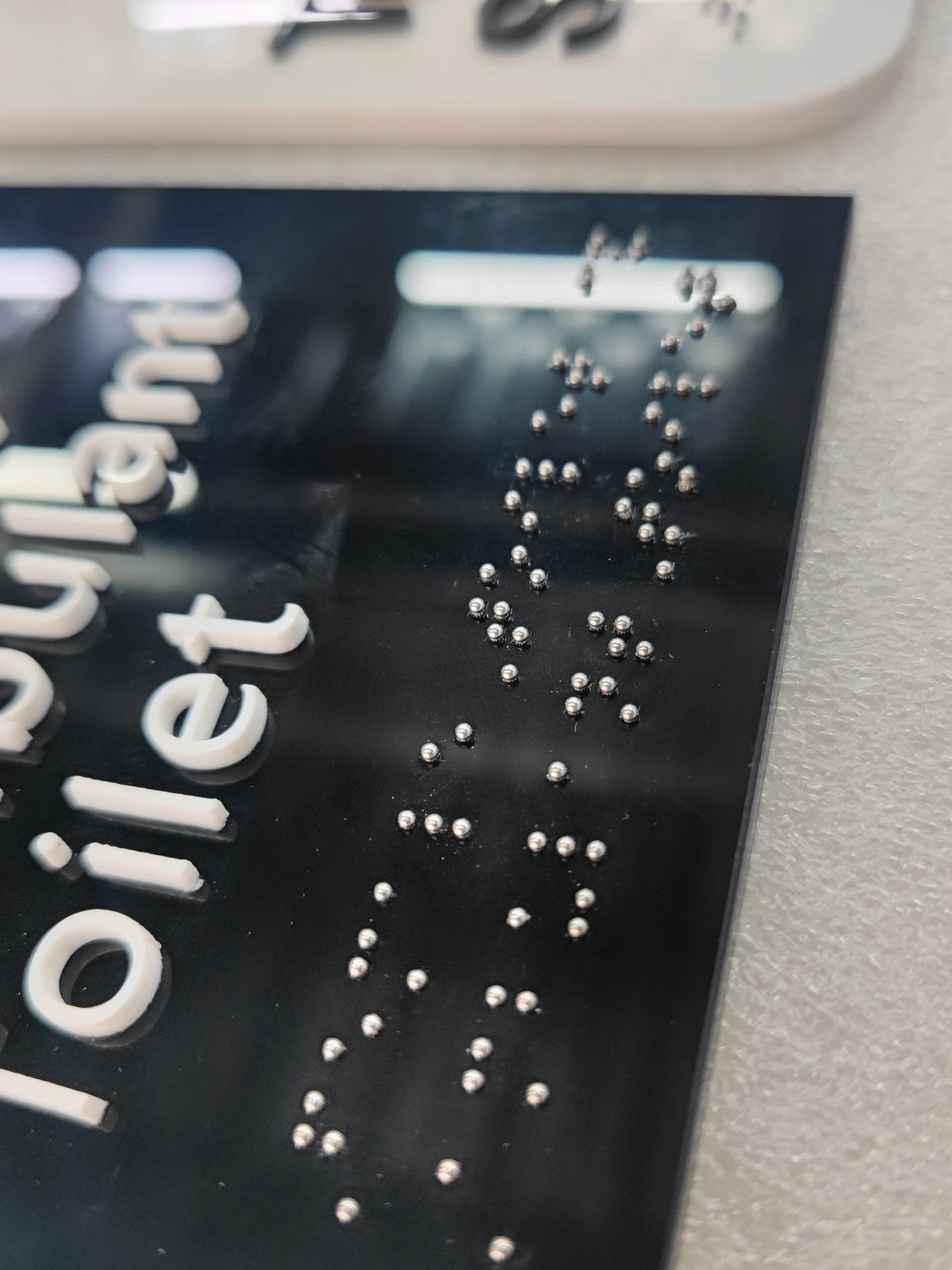 Interior Signs with 304 Stainless Steel Braille Studs — Close view of the completed black panel with raised white text, silver 304 stainless steel Braille studs, and a straight edge.