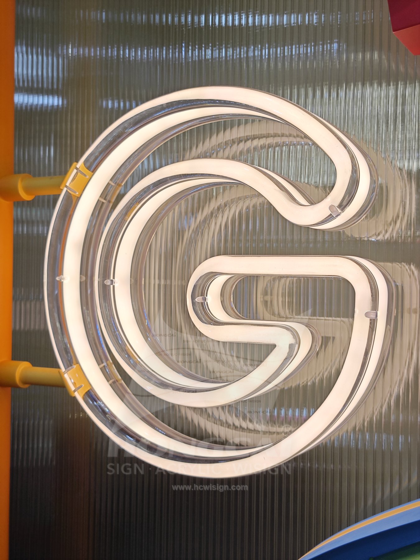 CNC-Machined Flame-Polished Acrylic G Sign — Completed crystal-clear acrylic G sign against a textured background